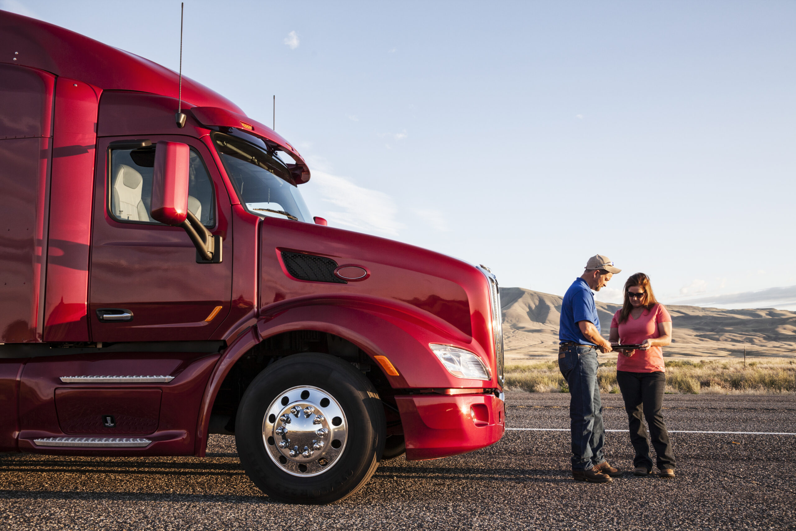 Husband and wife driving team checking their itinerary while standing in front of their commercial truck.